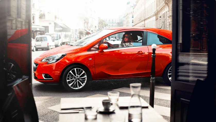 A woman is driving her orange Opel Corsa